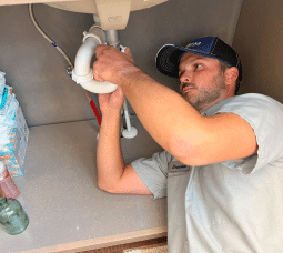 Plumber repairing a faucet beneath a bathroom sink.