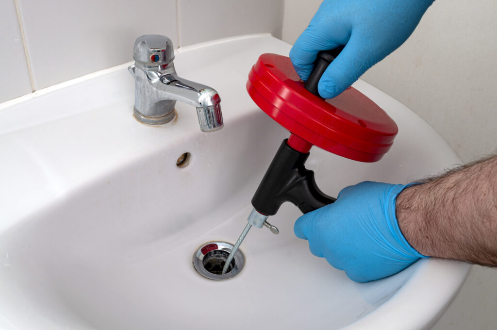 Plumber clearing sink drain clog in white bathroom sink.