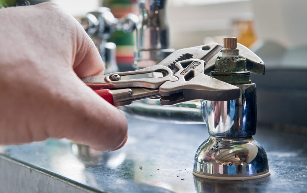 A plumber uses adjustable grips to remove a worn insert from a set of kitchen taps with a view to replace the damaged part.