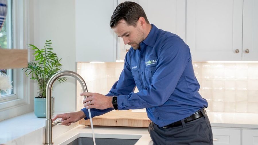Plumber inspecting a kitchen faucet during a residential plumbing service.